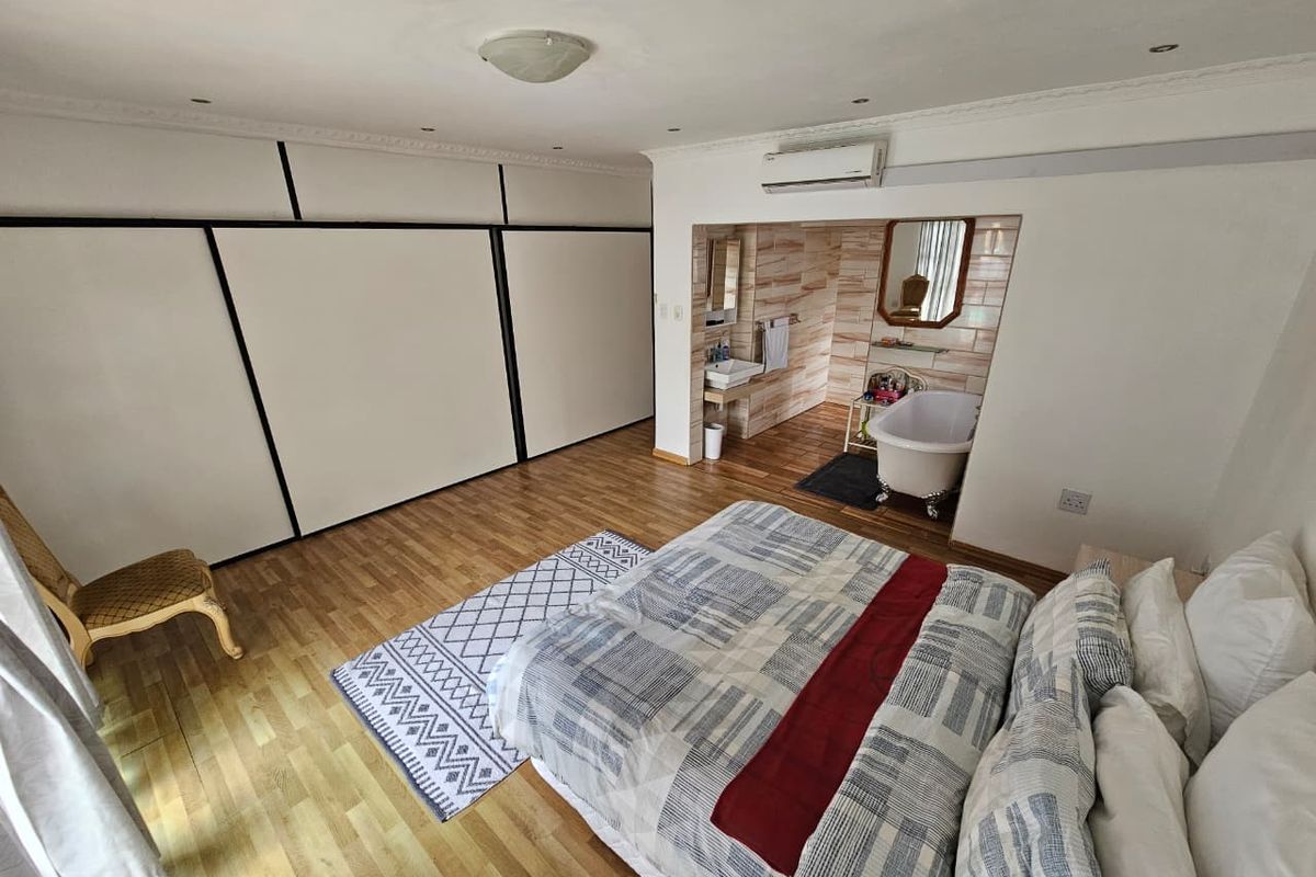 Spacious bedroom featuring built-in wardrobes, wood-look flooring, and an open-plan en-suite bathroom area with a freestanding bathtub and vanity.