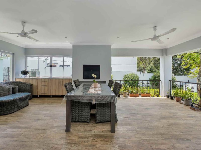Spacious covered patio featuring wood-look tiled flooring, built-in cabinetry, a fireplace, and ceiling fans, overlooking the garden.