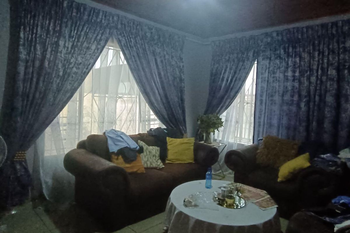 A living room featuring security bars on the windows and a timber ceiling, currently cluttered with personal items.