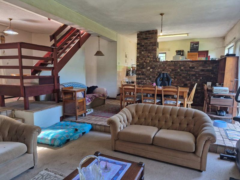 Open plan living and dining area featuring a prominent exposed brick wall and a timber staircase, offering a spacious layout with potential for modernization.