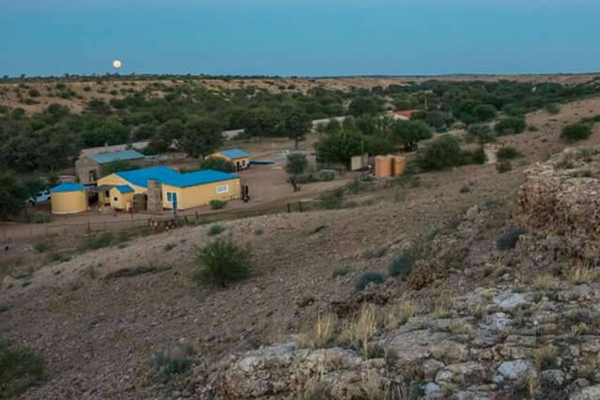An elevated aerial view of a rural small holding featuring multiple outbuildings, water storage tanks, and surrounding natural landscape at dusk.
