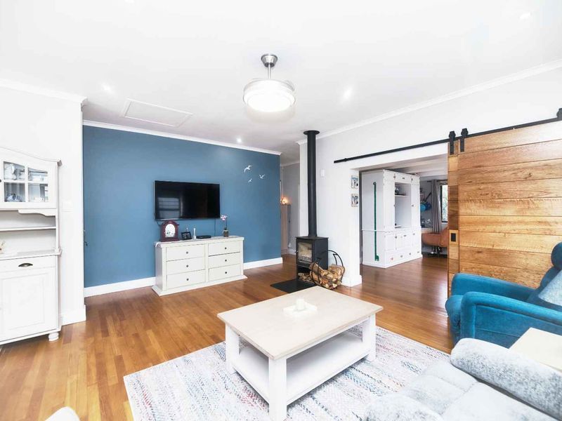 A bright living room featuring hardwood flooring, a freestanding wood-burning fireplace, and a distinctive sliding barn door leading to an adjacent space.