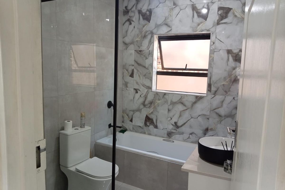 Modern bathroom featuring a bathtub with shower screen, contemporary vessel sink vanity, and stylish marble-effect wall tiling.