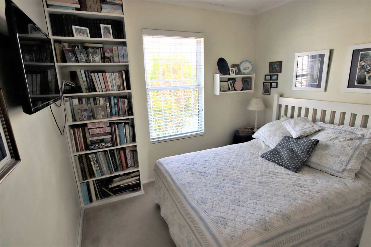 A cozy bedroom featuring neutral walls, carpeted flooring, and built-in shelving units, providing functional storage space and natural light through the window.
