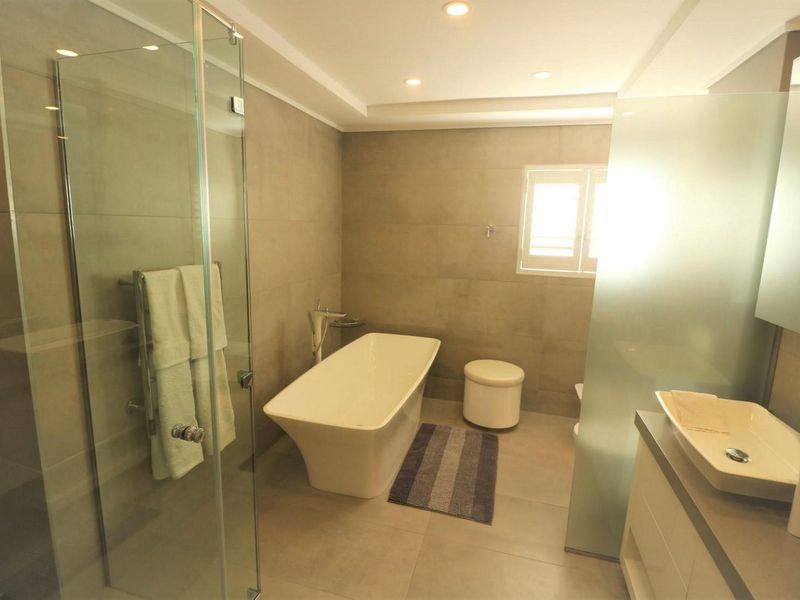 Modern bathroom featuring a freestanding bathtub, glass-enclosed shower, vessel sink vanity, and neutral floor-to-ceiling tiling with recessed lighting.