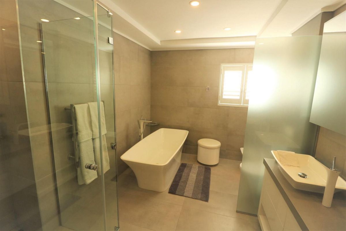 Modern bathroom featuring a freestanding bathtub, glass-enclosed shower, vessel sink vanity, and neutral floor-to-ceiling tiling with recessed lighting.