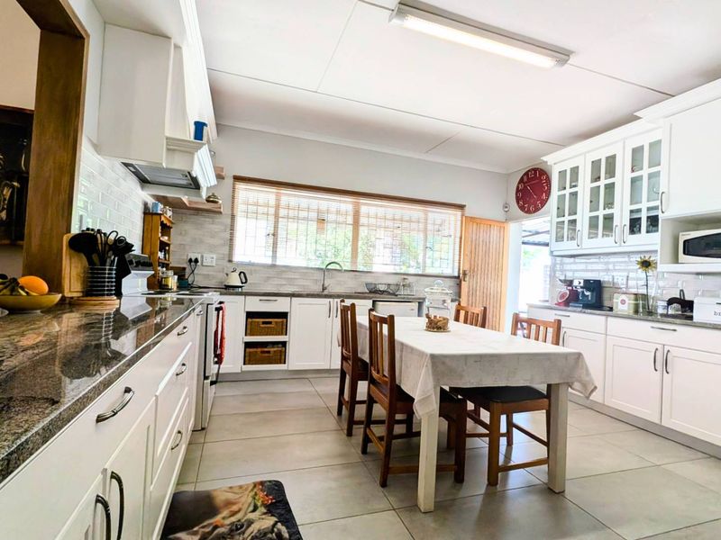 Spacious kitchen featuring white shaker cabinetry, granite countertops, subway tile backsplash, and integrated appliances with ample space for a dining table.