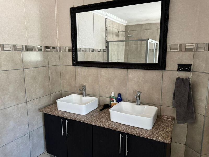 A modern bathroom featuring a double vanity with vessel sinks, granite-look countertop, and a glass-enclosed shower.