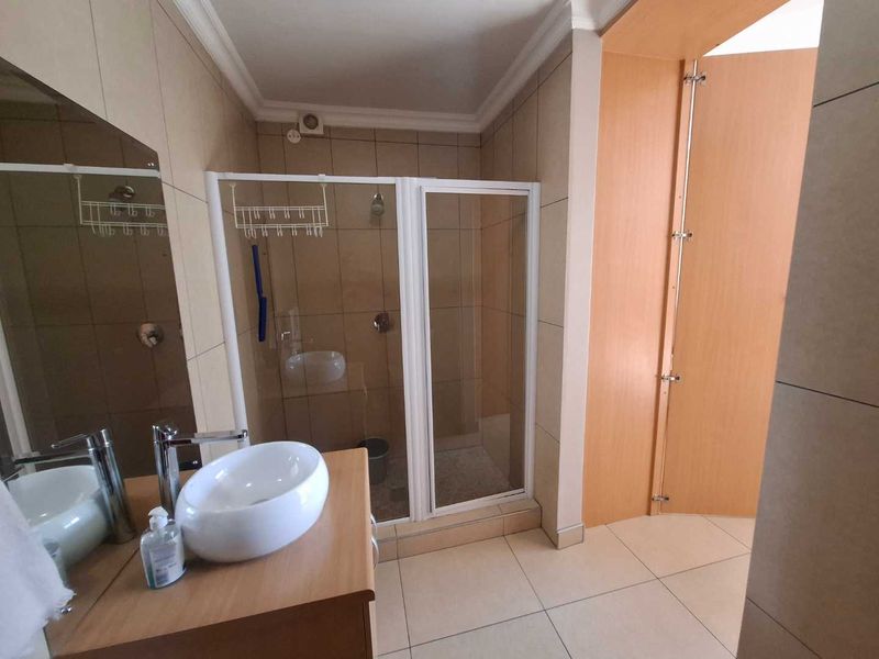A modern bathroom featuring a tiled shower enclosure, a contemporary vessel sink set on a vanity cabinet, and neutral wall and floor tiling.