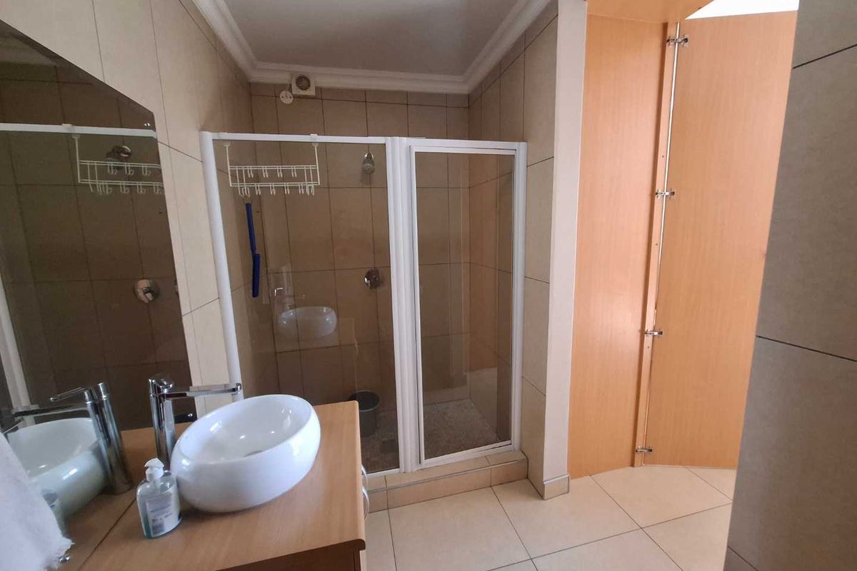 A modern bathroom featuring a tiled shower enclosure, a contemporary vessel sink set on a vanity cabinet, and neutral wall and floor tiling.