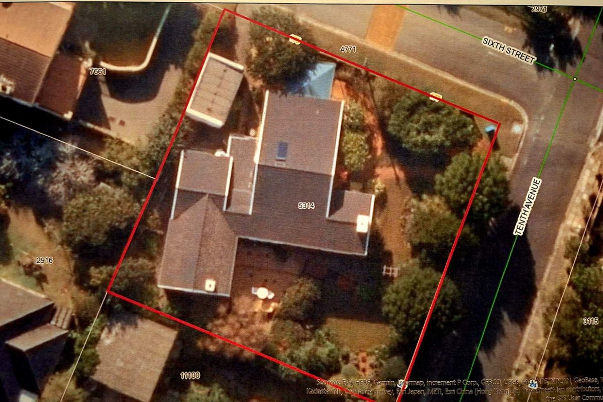 An aerial satellite view of the property showing the roof layout, chimney, skylight, and surrounding garden area on a corner lot.