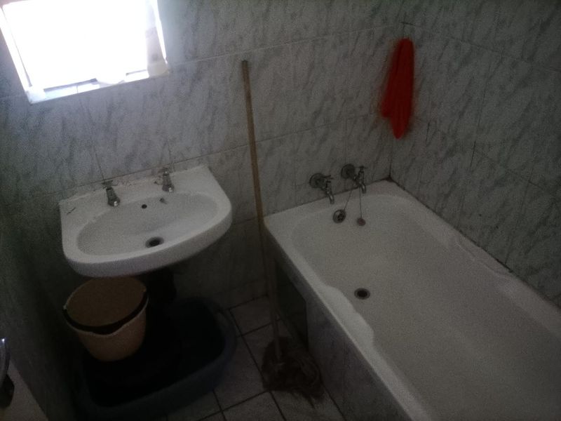 A dated bathroom featuring a standard pedestal washbasin and bathtub with wall-to-floor tiling, requiring modernization to improve aesthetic appeal and functionality.