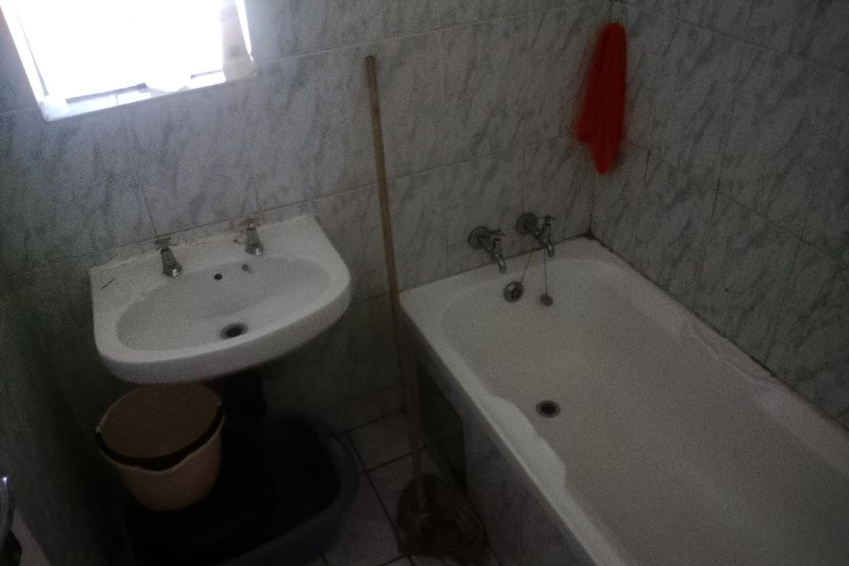 A dated bathroom featuring a standard pedestal washbasin and bathtub with wall-to-floor tiling, requiring modernization to improve aesthetic appeal and functionality.