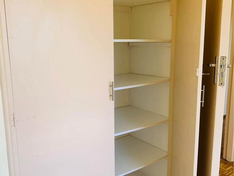 A built-in storage cupboard with multiple shelves, featuring parquet flooring in the surrounding area.