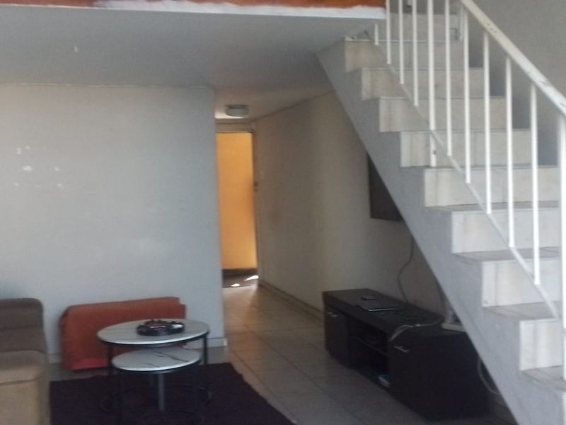 Open plan living area featuring a staircase leading to a mezzanine level, tiled flooring, and neutral wall finishes.