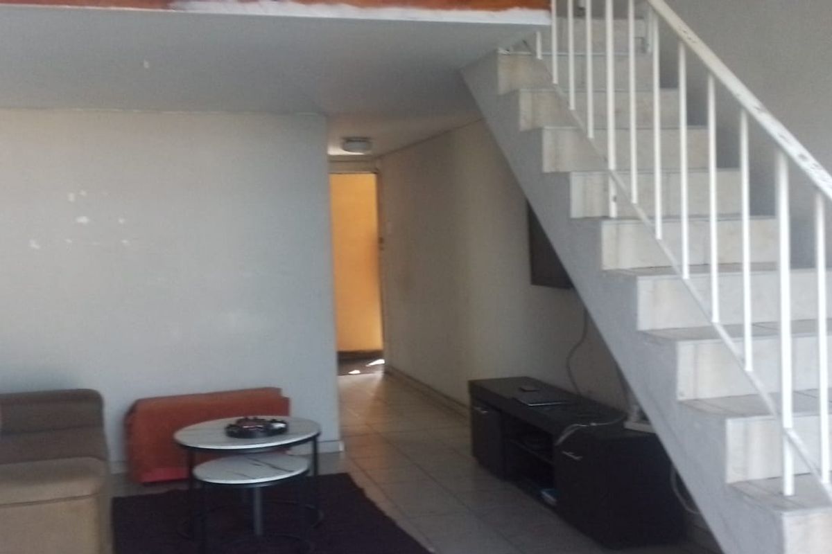 Open plan living area featuring a staircase leading to a mezzanine level, tiled flooring, and neutral wall finishes.