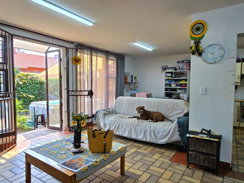 Open-plan living area featuring tiled floors and direct access to the patio, adjacent to a functional kitchen with built-in cabinetry and appliances.