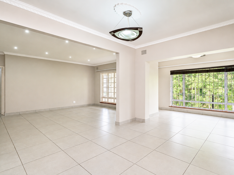 Spacious, light-filled open-plan living area featuring neutral tiled flooring, recessed lighting, and large windows with security bars, offering a versatile blank canvas.