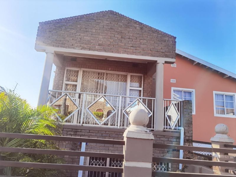 Front elevation of a brick house featuring a covered balcony with decorative metal balustrades and security gates.