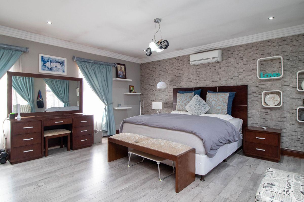 Spacious bedroom featuring light wood-look flooring, a textured stone-effect feature wall, recessed ceiling lighting, and a wall-mounted air conditioning unit.