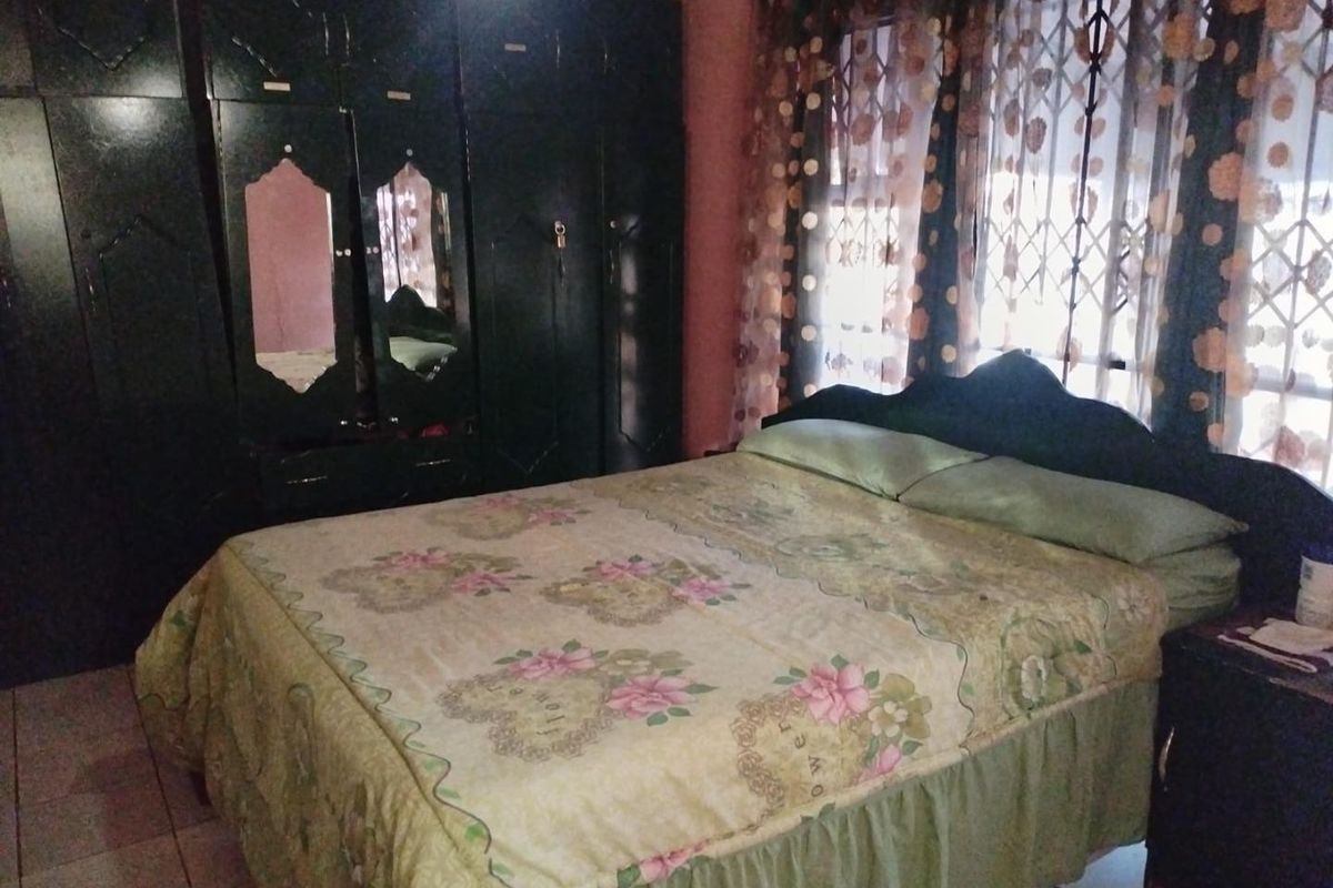 A bedroom featuring built-in cupboards, tiled flooring, and a security gate on the window.