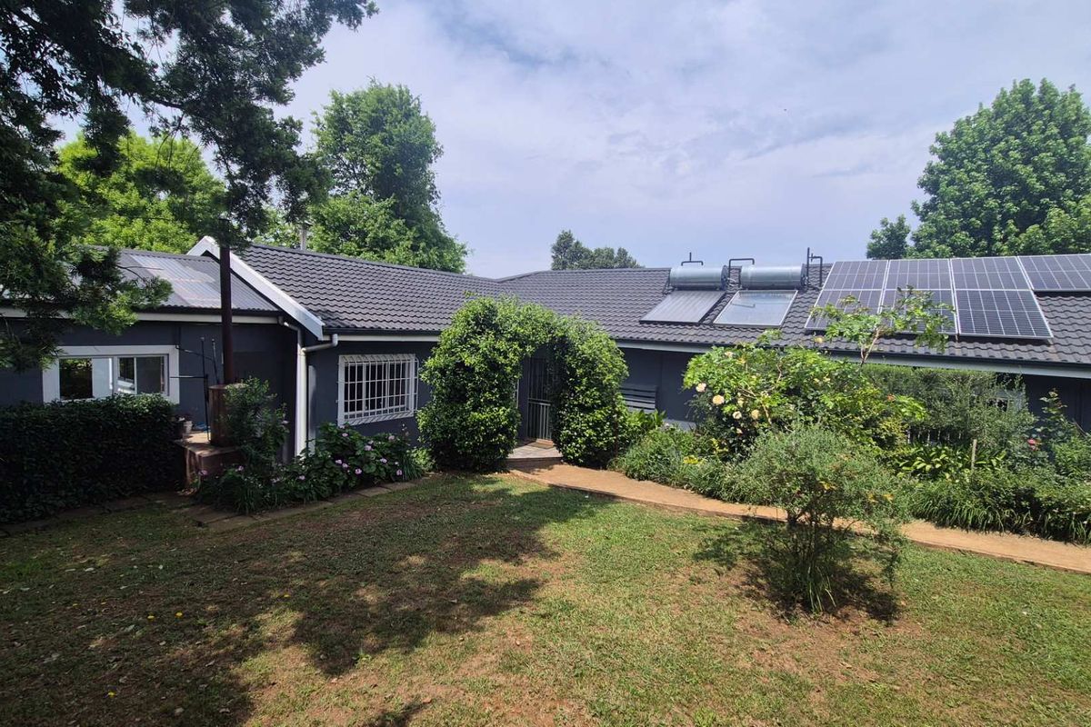 Rear view of the property featuring a well-maintained garden, paved walkway, and roof-mounted solar panels and solar water heating system.