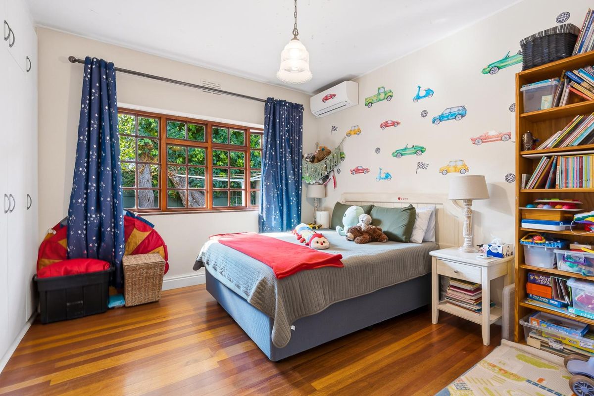 A bedroom featuring polished timber flooring, a large multi-pane window, and a wall-mounted air conditioning unit.