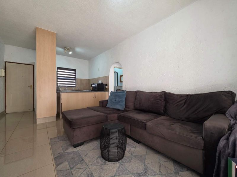 Open plan living area featuring tiled floors, textured walls, and a compact kitchen space with built-in cabinetry.