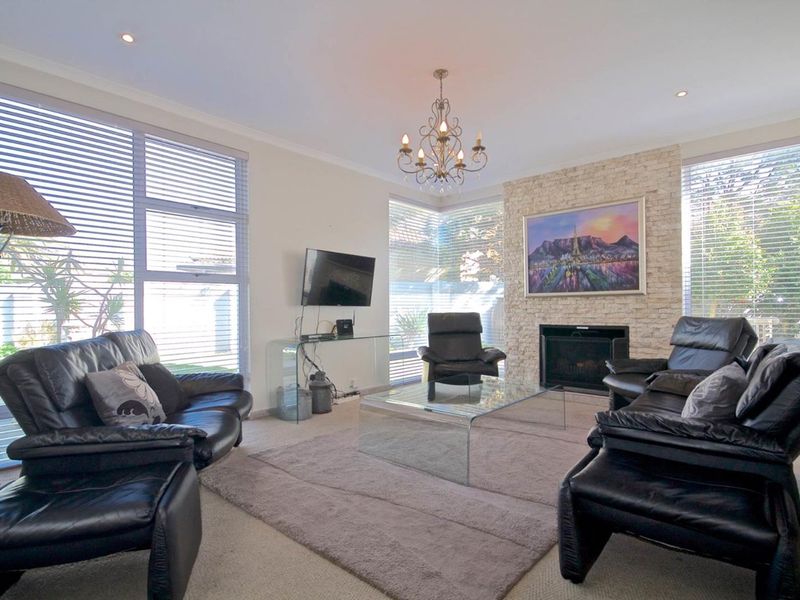 Spacious living room featuring a prominent stone-clad fireplace, large windows with venetian blinds, and recessed downlighting, creating a bright and comfortable atmosphere.