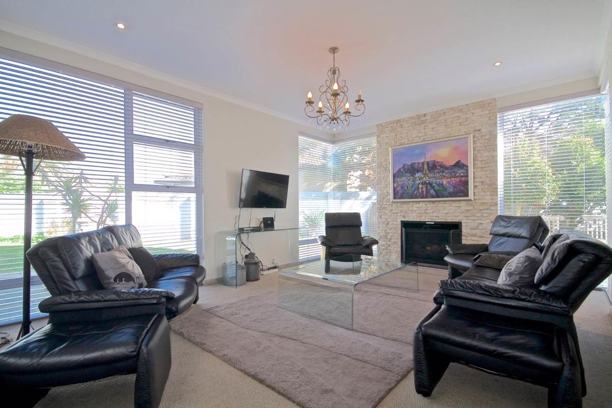 Spacious living room featuring a prominent stone-clad fireplace, large windows with venetian blinds, and recessed downlighting, creating a bright and comfortable atmosphere.