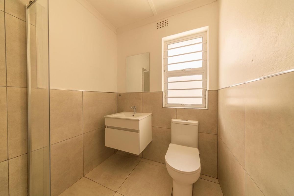A clean, modern bathroom featuring a wall-mounted vanity, a toilet, and a glass-enclosed shower with neutral floor-to-ceiling tiling.