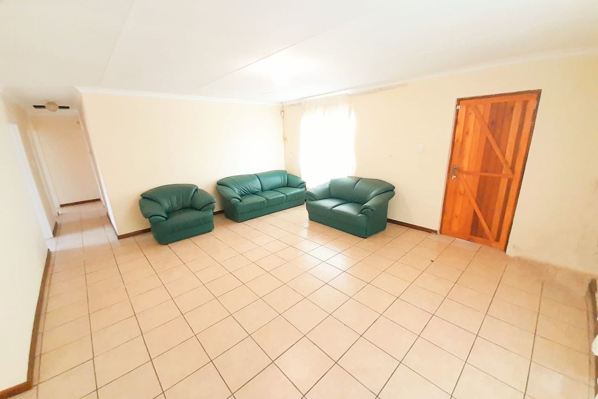 A spacious living room featuring neutral ceramic floor tiles and a solid timber door, offering a blank canvas for interior design.