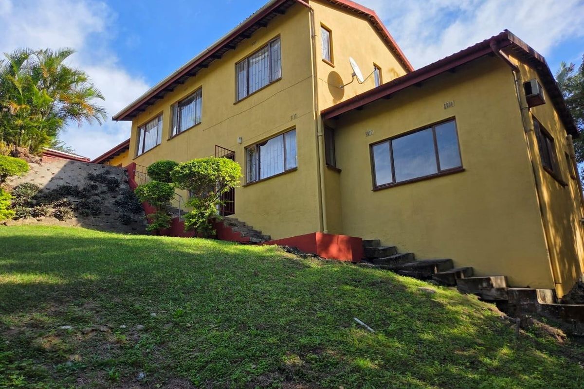 Rear view of a two-story house featuring yellow exterior walls, metal security bars on windows, and concrete stairs leading up the sloped garden.