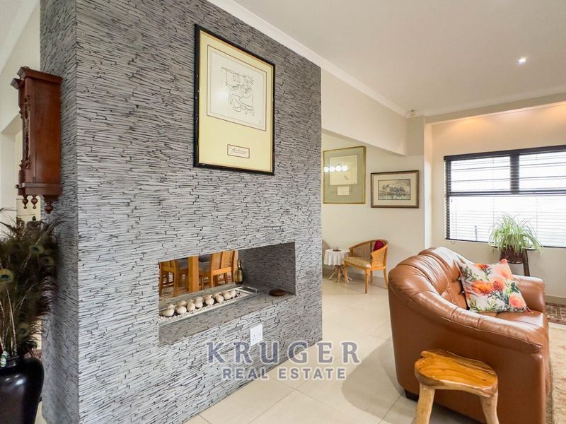 A spacious living room featuring a prominent stone-clad double-sided fireplace and neutral tiled flooring, creating a warm and inviting atmosphere.