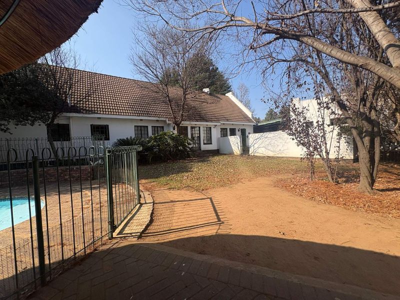 Rear view of the farmhouse featuring a tiled roof, a fenced swimming pool, and a paved patio area overlooking the garden.