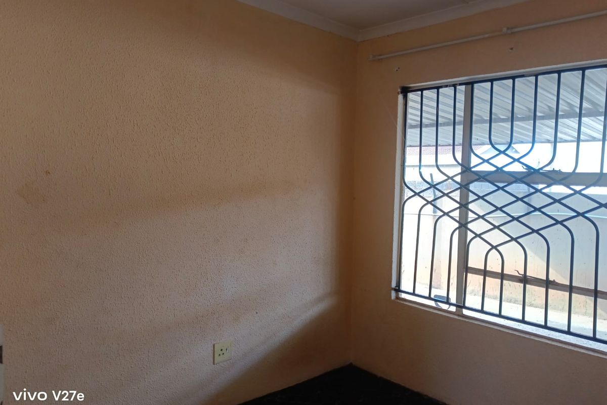 An empty bedroom featuring a window with a security gate and standard electrical outlets, requiring cosmetic updates to the wall finishes.