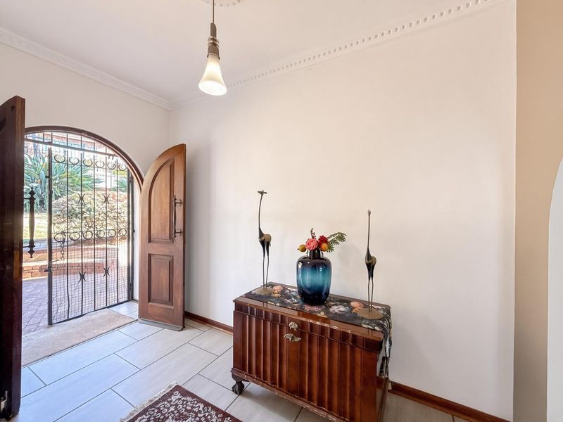 Welcoming entrance hall featuring an arched wooden front door, wrought iron security gate, tiled flooring, and decorative ceiling cornice.