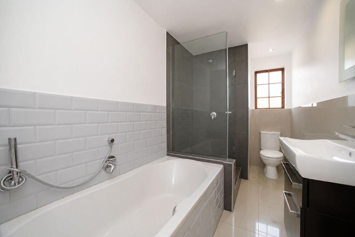 A modern bathroom featuring a bathtub, separate glass-enclosed shower, toilet, and a vanity basin with contemporary tiling.