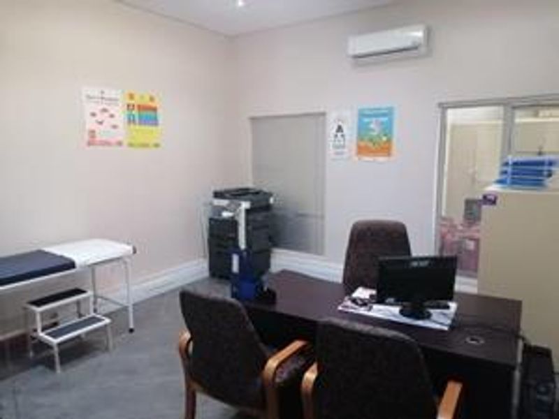 A functional office space featuring a wall-mounted air conditioning unit, roller blinds, and a glass partition, suitable for professional use.