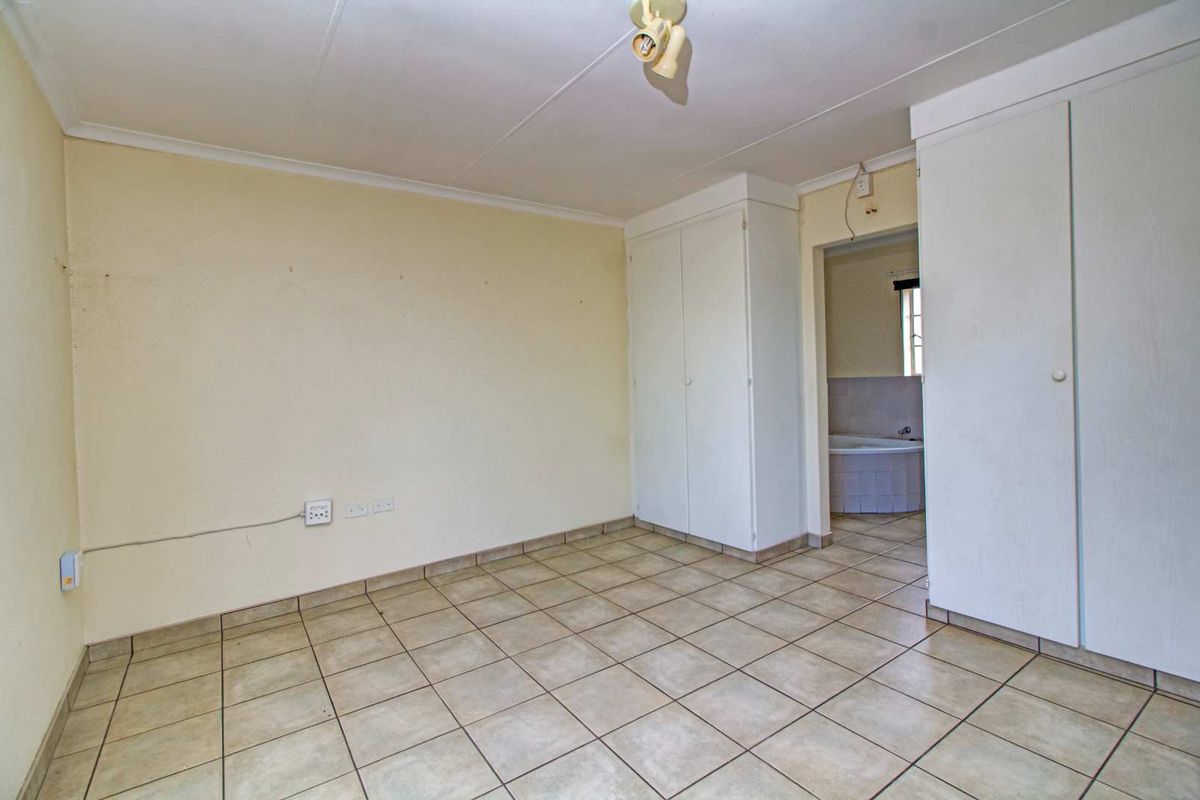A vacant bedroom featuring tiled flooring, built-in cupboards, and an adjoining en-suite bathroom area.