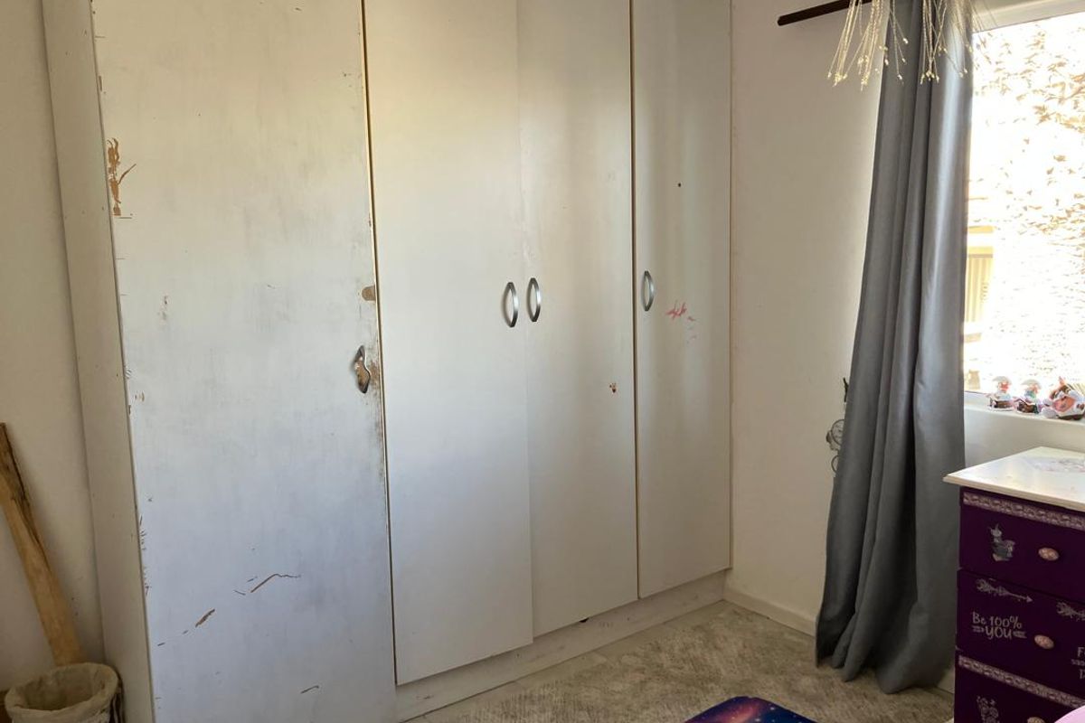 A bedroom featuring a large built-in wardrobe with visible signs of wear and surface damage on the doors.
