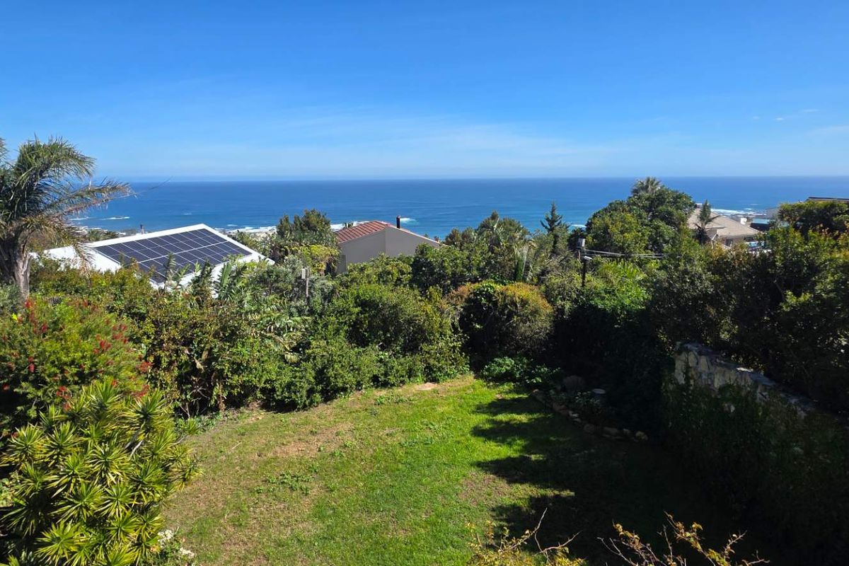 Elevated view overlooking a lush garden with a stone retaining wall, featuring a clear ocean horizon and neighbouring properties with solar installations.