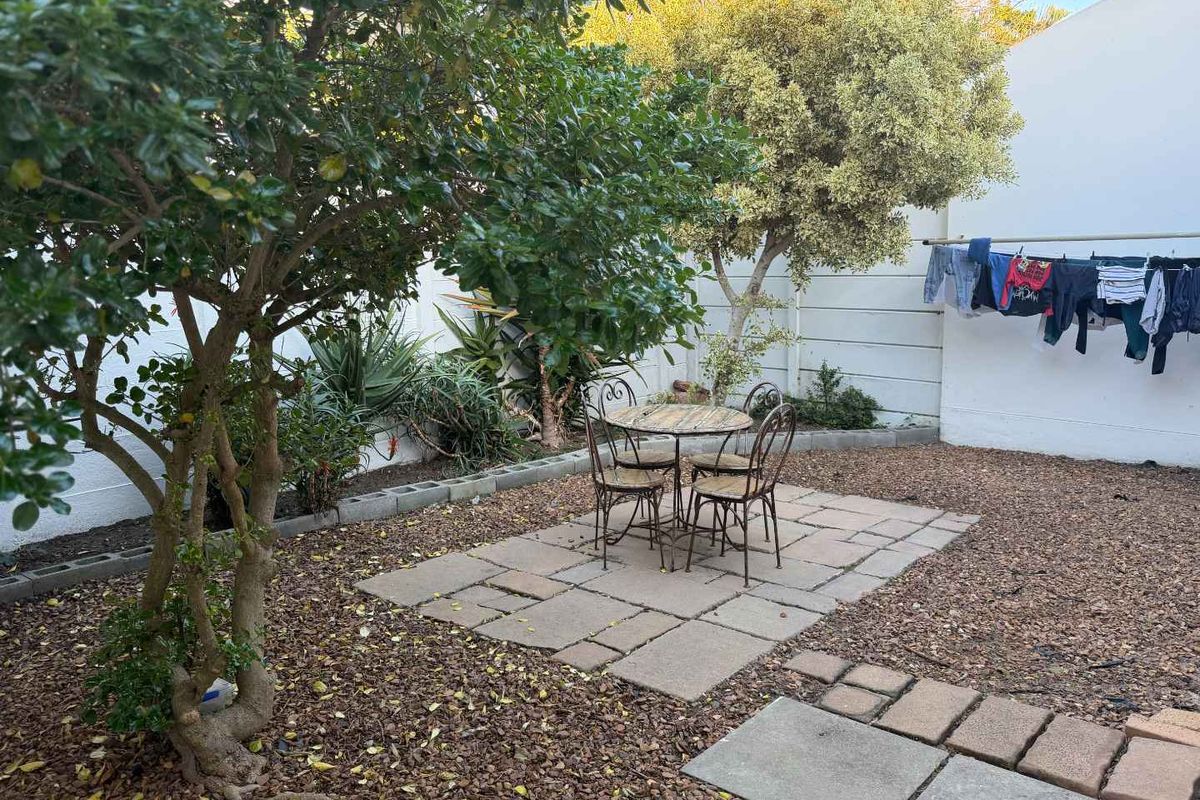 A private rear garden featuring a paved patio area, established trees, and perimeter walling, providing a functional outdoor space.