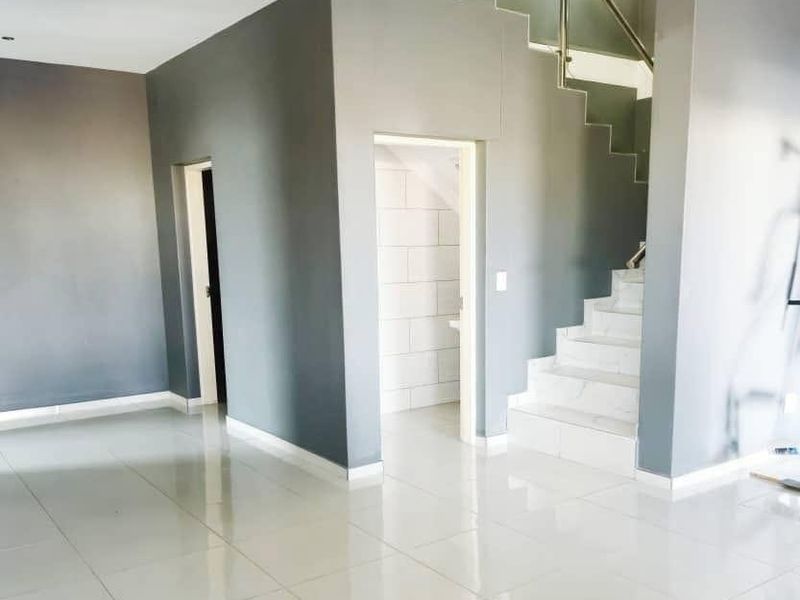 An open-plan living area featuring modern tiled flooring, a staircase with a glass balustrade, and neutral grey wall finishes.
