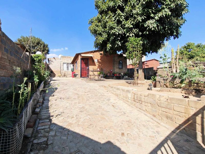 A rear exterior view of the property featuring a cobblestone driveway, brick retaining wall, and a secure entrance.