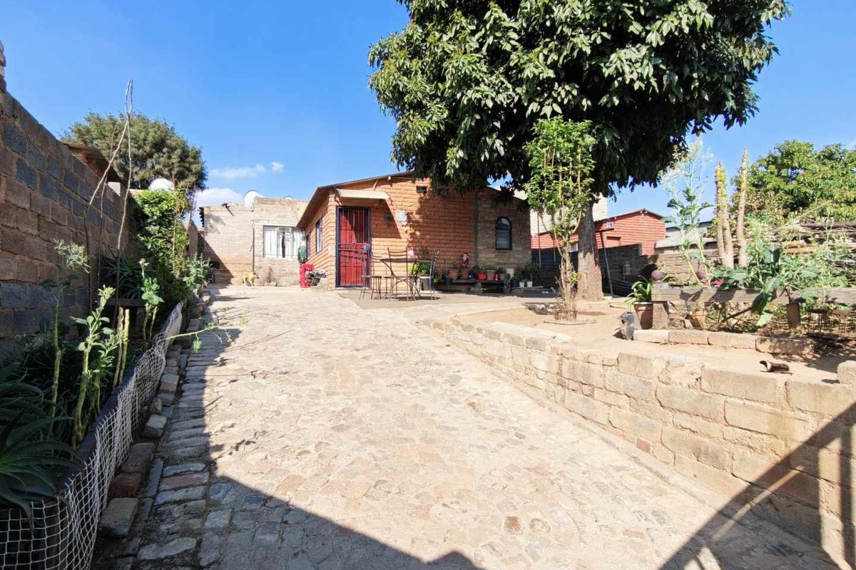 A rear exterior view of the property featuring a cobblestone driveway, brick retaining wall, and a secure entrance.