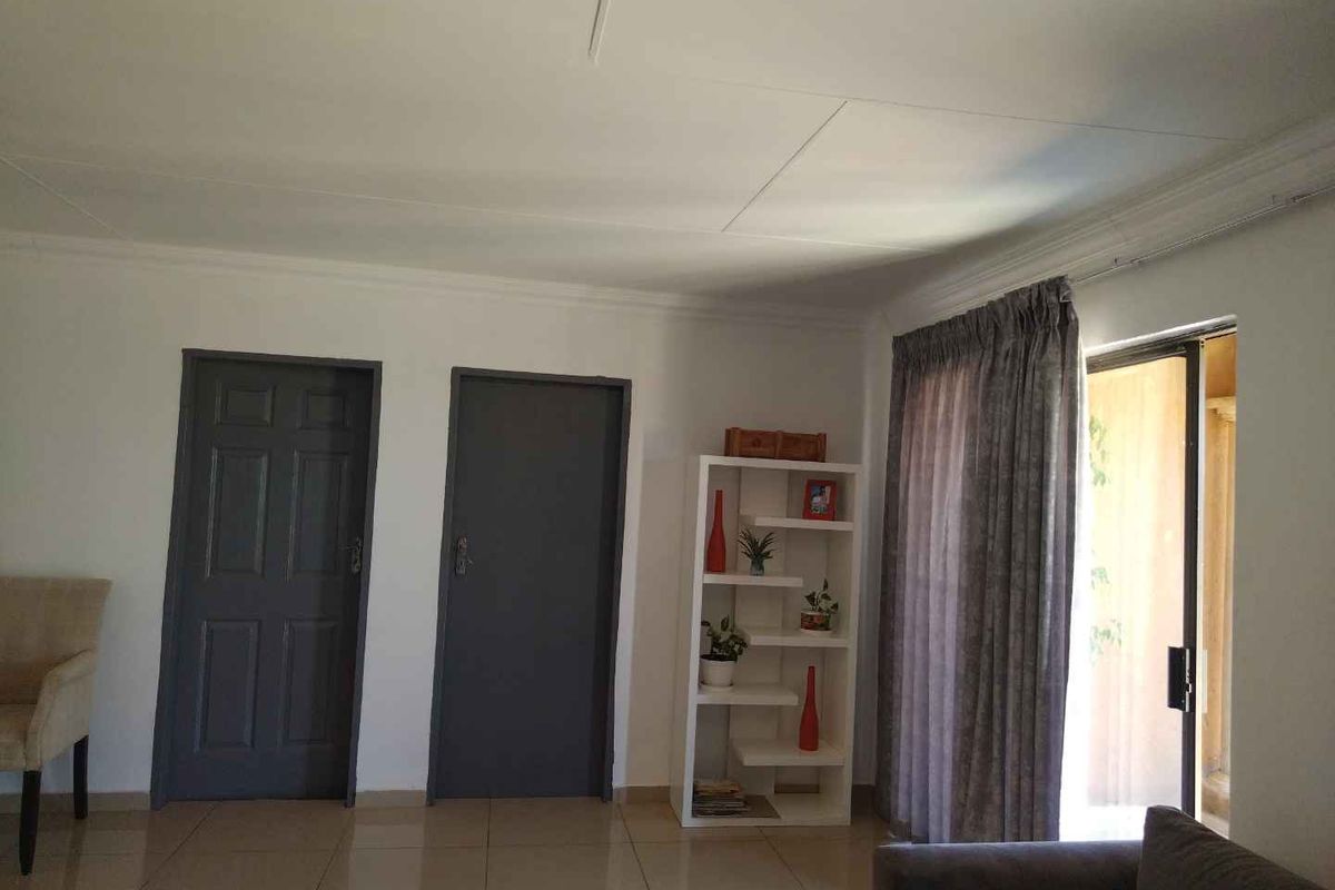 A living room featuring tiled flooring, two dark-toned interior doors, and a sliding glass door providing access to an outdoor area.