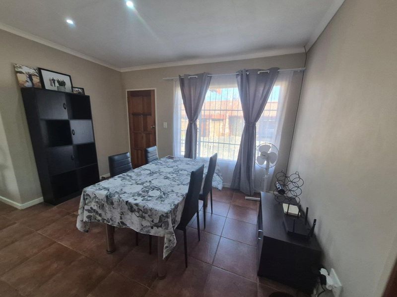 A functional dining room featuring tiled flooring, recessed downlighting, and a window fitted with security bars, providing a practical space for meals.
