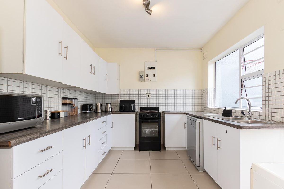 A functional kitchen featuring white cabinetry, dark laminate countertops, tiled splashbacks, and a stainless steel sink with a window view.