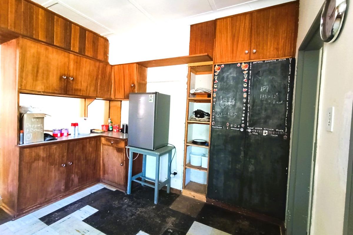 A dated kitchen area featuring extensive wooden cabinetry, open shelving, and a chalkboard panel, offering potential for a modern renovation.